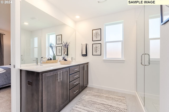 ensuite bathroom with double vanity, a stall shower, a sink, ensuite bath, and baseboards