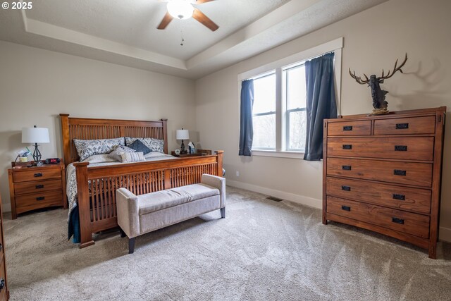 bedroom featuring ceiling fan, a tray ceiling, and light carpet