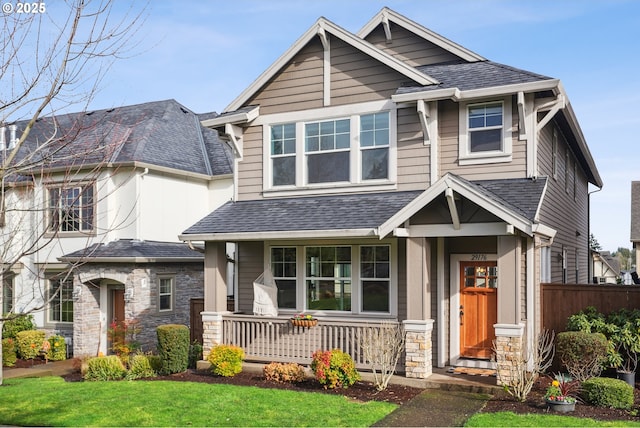 craftsman inspired home featuring stone siding, a shingled roof, a front yard, and fence