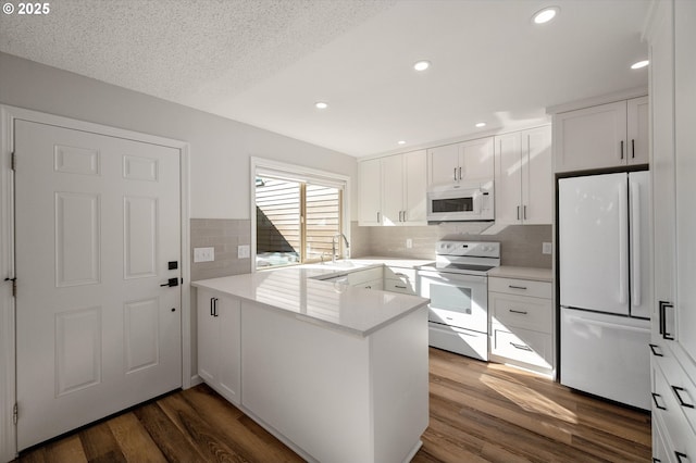 kitchen featuring dark wood-style floors, white cabinets, a sink, white appliances, and a peninsula