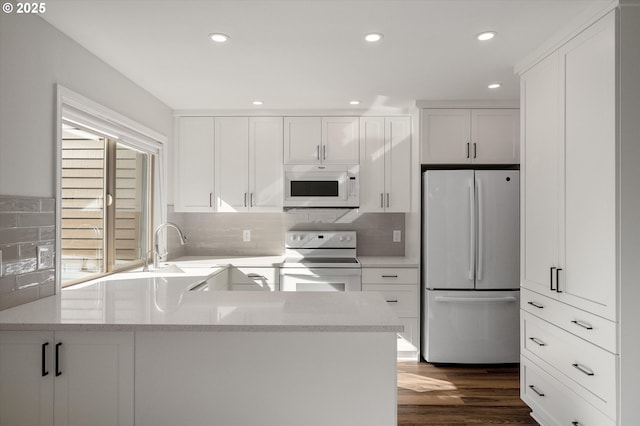 kitchen with white appliances, white cabinets, dark wood-style floors, a sink, and backsplash