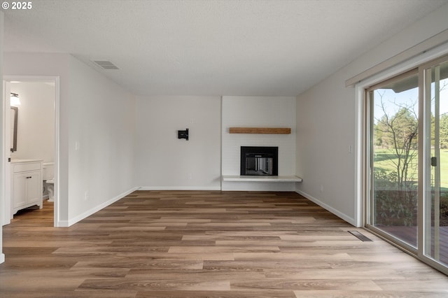 unfurnished living room with a brick fireplace, a textured ceiling, baseboards, and wood finished floors