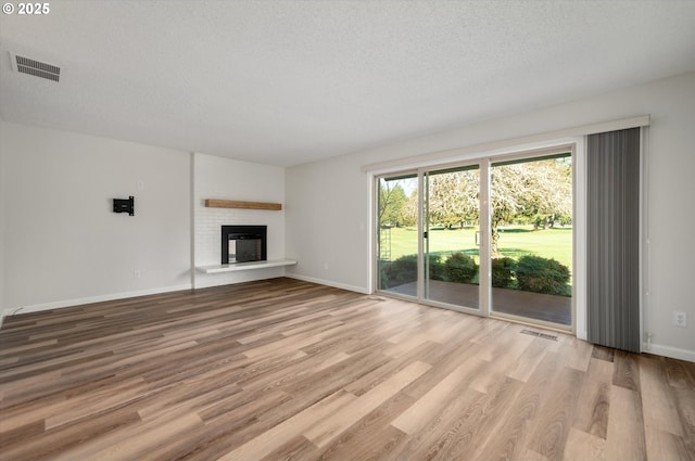 unfurnished living room featuring light wood finished floors, a glass covered fireplace, and visible vents