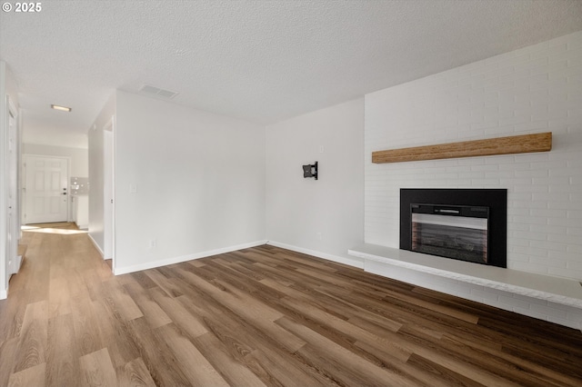 unfurnished living room featuring a brick fireplace, a textured ceiling, visible vents, and wood finished floors