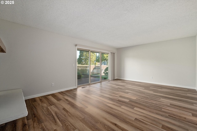 empty room with wood finished floors, visible vents, and baseboards