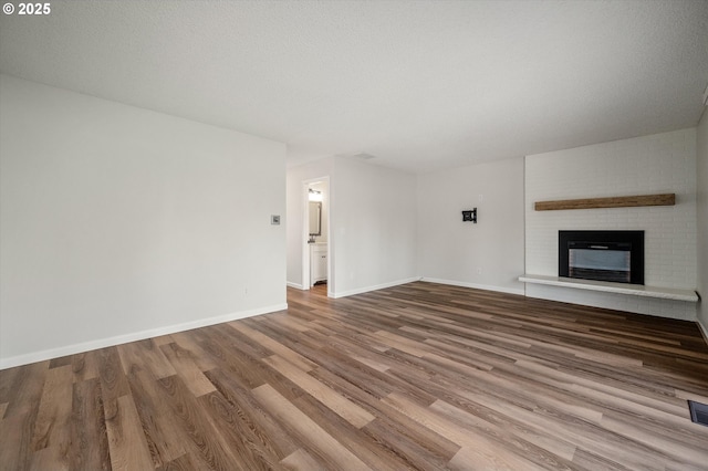 unfurnished living room featuring visible vents, baseboards, wood finished floors, a textured ceiling, and a brick fireplace