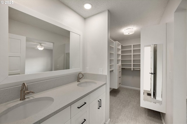 bathroom featuring a textured ceiling, a spacious closet, double vanity, and a sink