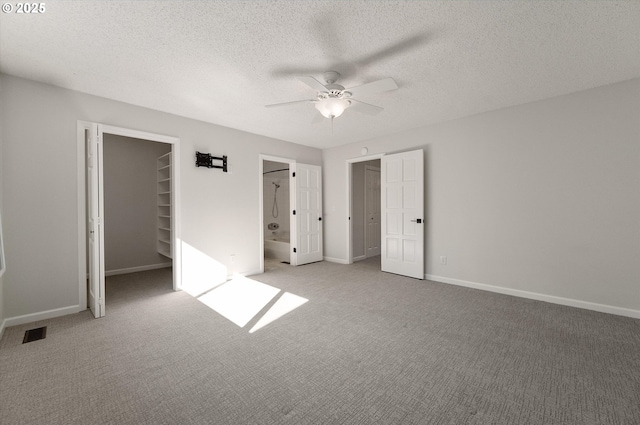 unfurnished bedroom with carpet, a closet, a spacious closet, a textured ceiling, and baseboards