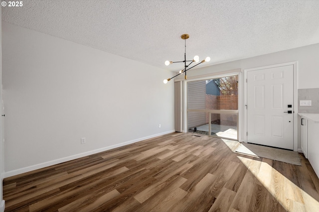 unfurnished dining area featuring baseboards, a textured ceiling, wood finished floors, and an inviting chandelier