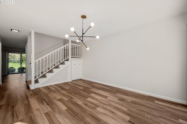 interior space featuring a textured ceiling, wood finished floors, baseboards, stairway, and an inviting chandelier