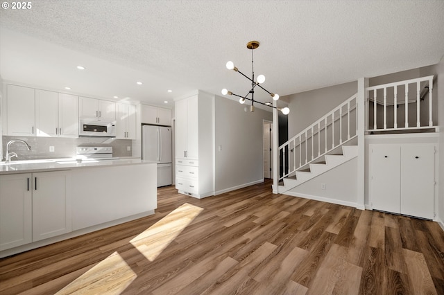 kitchen with white appliances, a sink, white cabinetry, and light wood-style floors