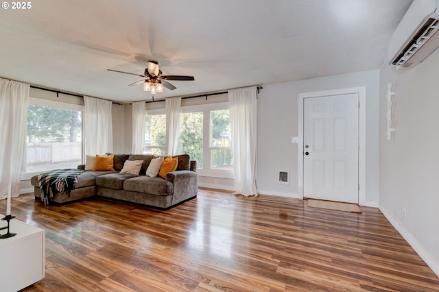 living room with ceiling fan, an AC wall unit, wood finished floors, and baseboards