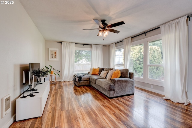 living room with baseboards, light wood-style flooring, and a ceiling fan