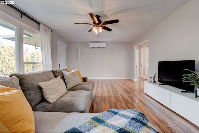 living room featuring light wood finished floors, a wall unit AC, a ceiling fan, and baseboards