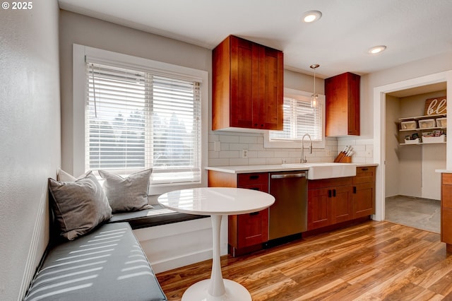 kitchen featuring decorative backsplash, dishwasher, light wood-style flooring, pendant lighting, and a sink