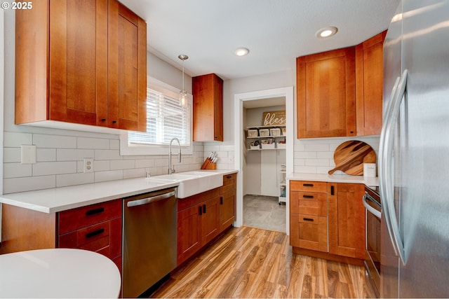 kitchen featuring tasteful backsplash, light countertops, appliances with stainless steel finishes, light wood-style floors, and a sink