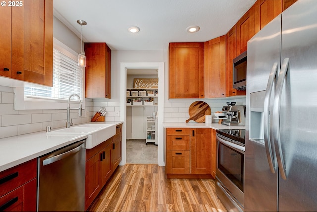 kitchen featuring tasteful backsplash, light countertops, light wood-style flooring, appliances with stainless steel finishes, and a sink