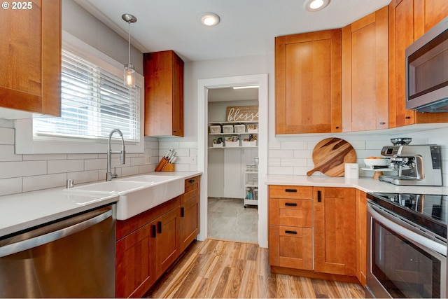 kitchen with stainless steel appliances, light countertops, hanging light fixtures, light wood-style floors, and a sink