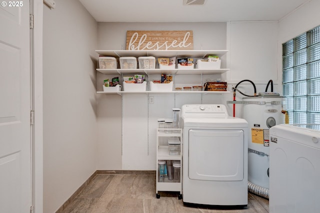 clothes washing area with laundry area, visible vents, baseboards, strapped water heater, and washer and dryer