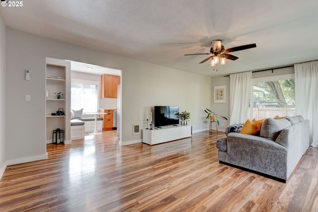 living area featuring light wood-style floors, ceiling fan, baseboards, and a textured ceiling