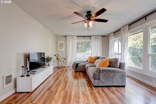 living area with light wood-style floors, baseboards, ceiling fan, and heating unit