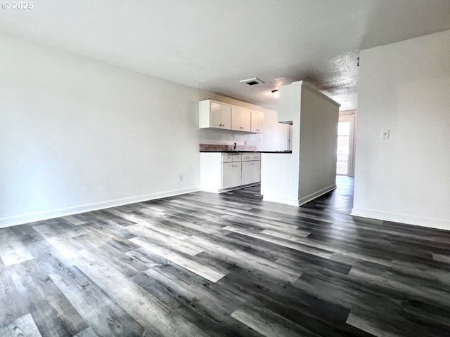 unfurnished living room featuring dark wood finished floors, visible vents, and baseboards