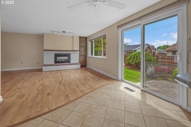 unfurnished living room with track lighting, ceiling fan, a textured ceiling, baseboards, and a brick fireplace