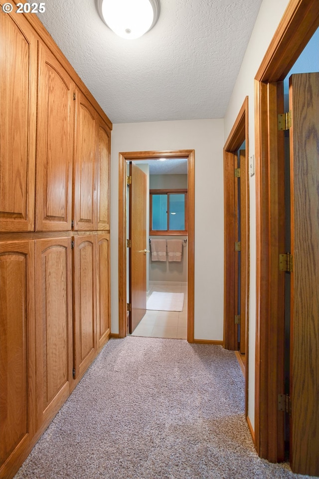 hallway featuring light colored carpet and a textured ceiling