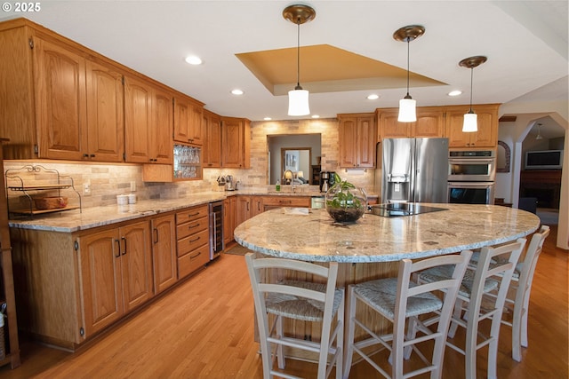 kitchen with a tray ceiling, a kitchen breakfast bar, a kitchen island, stainless steel appliances, and beverage cooler