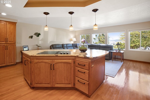 kitchen with pendant lighting, black electric cooktop, a kitchen island, and light wood-type flooring