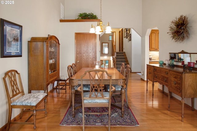 dining area featuring a towering ceiling, a chandelier, and light wood-type flooring