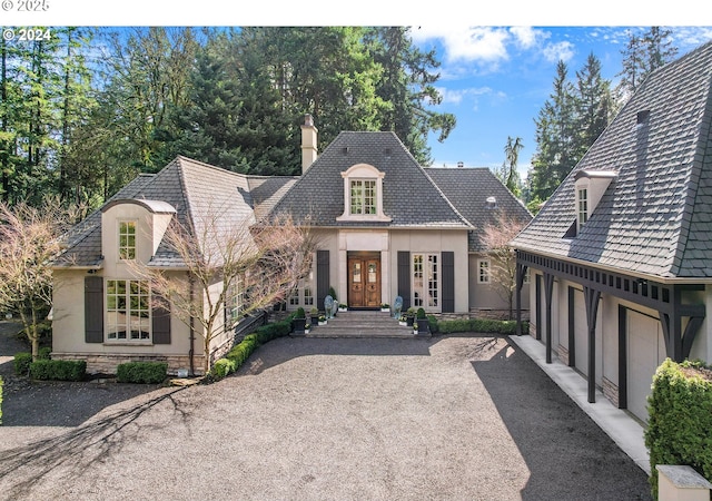 french country home with stone siding, a chimney, aphalt driveway, french doors, and stucco siding