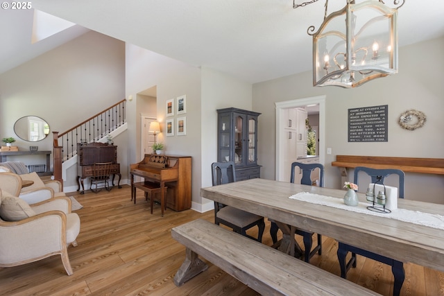 dining room featuring an inviting chandelier, stairs, light wood finished floors, and high vaulted ceiling
