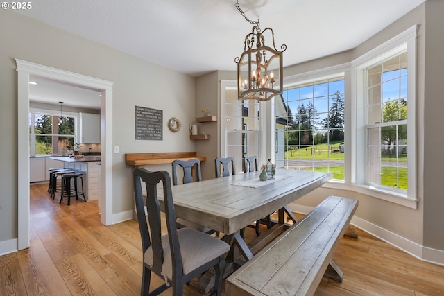 dining area with an inviting chandelier, baseboards, and light wood-type flooring