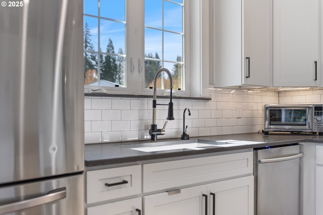 kitchen featuring a sink, appliances with stainless steel finishes, decorative backsplash, and dark countertops