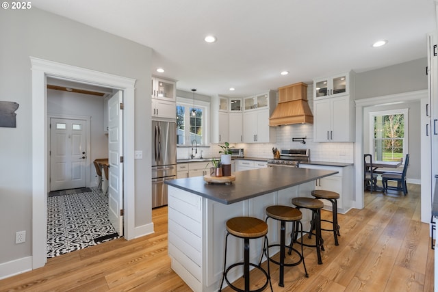kitchen featuring light wood-style flooring, custom exhaust hood, dark countertops, and stainless steel appliances