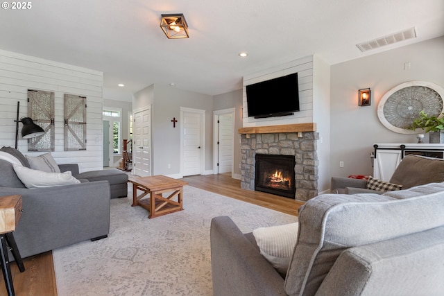 living room with visible vents, wood finished floors, baseboards, a stone fireplace, and recessed lighting