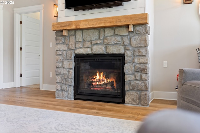 interior details featuring baseboards, a stone fireplace, and wood finished floors