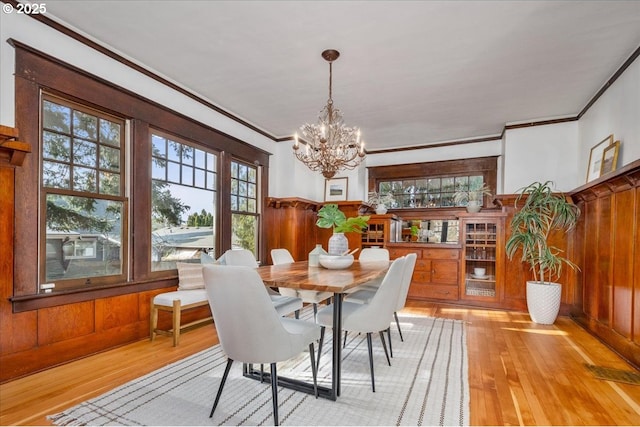 dining area with crown molding, an inviting chandelier, wooden walls, and light hardwood / wood-style flooring