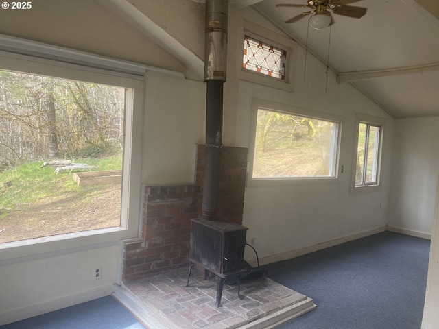 unfurnished sunroom featuring vaulted ceiling, plenty of natural light, a wood stove, and a ceiling fan