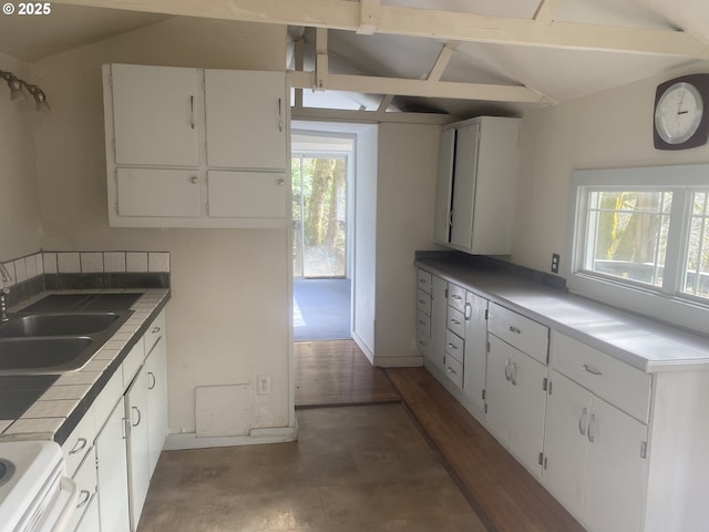 kitchen featuring tile counters, white cabinets, vaulted ceiling, a sink, and range