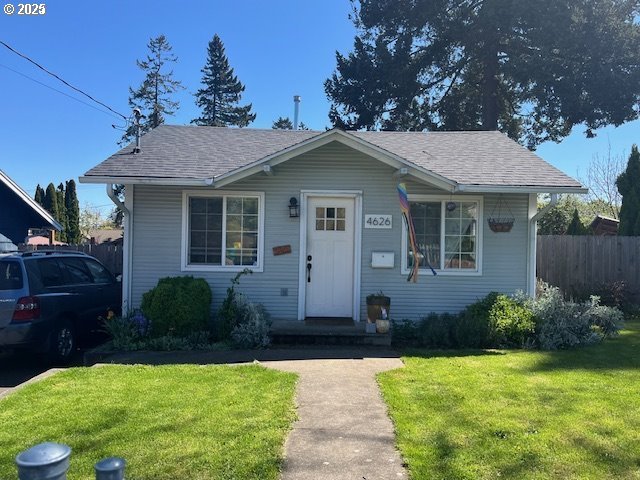 bungalow-style house featuring a front lawn, a shingled roof, and fence