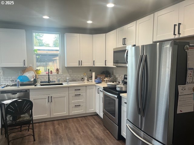 kitchen featuring dark wood-style flooring, a sink, white cabinets, light countertops, and appliances with stainless steel finishes