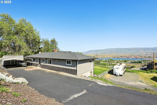 view of front facade featuring a water and mountain view, stone siding, and a chimney