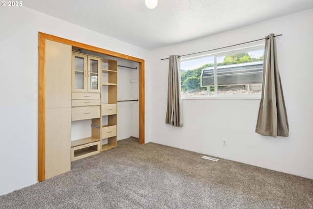 unfurnished bedroom with carpet, a closet, a textured ceiling, and visible vents