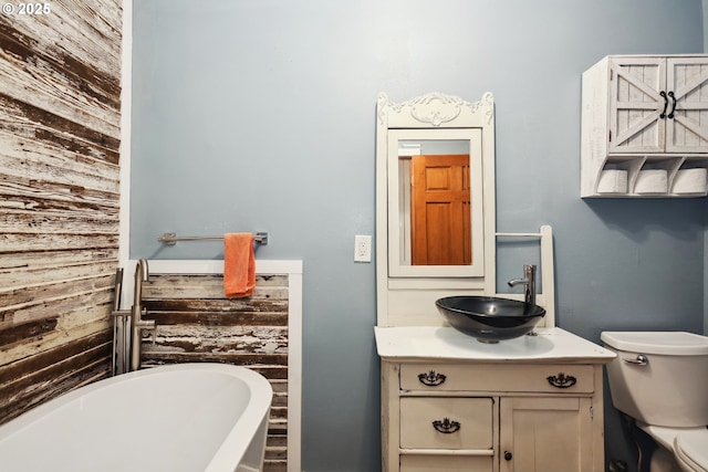 bathroom featuring vanity, wood walls, a freestanding bath, and toilet