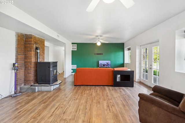 living room featuring ceiling fan, visible vents, a wood stove, and light wood-style floors