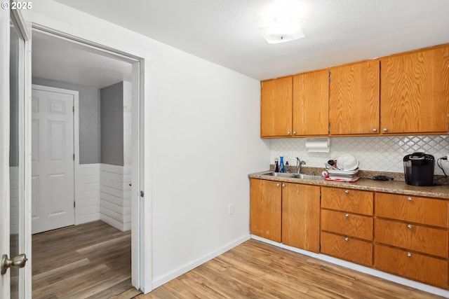 kitchen with a sink, decorative backsplash, brown cabinetry, and light wood-type flooring