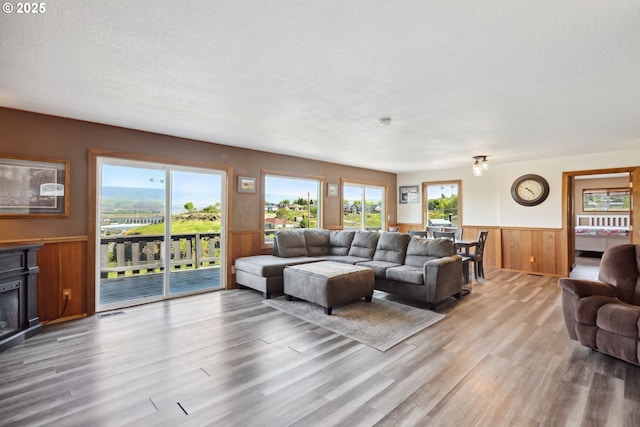 living area featuring light wood-type flooring, a textured ceiling, wainscoting, and wood walls
