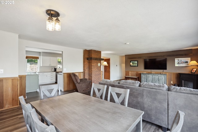 dining space featuring wooden walls, a textured ceiling, wainscoting, and dark wood-type flooring